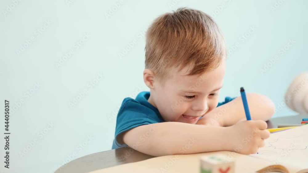 A smiling little child with down syndrome drawing something with a marker at home A smiling little child with down syndrome drawing something with a marker at home