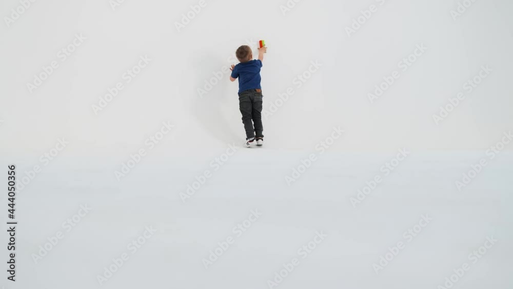 A rear view of a little boy with down syndrome driving a constructor along the walls in the white studio A rear view of a little boy with down syndrome driving a constructor along the walls in the white studio