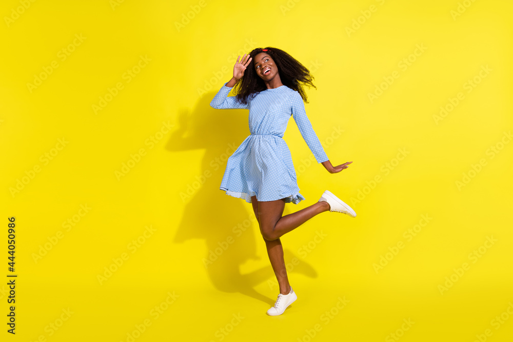 Full length body size photo of dancing girl in blue dotted dress looking empty space relaxing at party isolated bright yellow color background Full length body size photo of dancing girl in blue dotted dress looking empty space relaxing at party isolated bright yellow color background