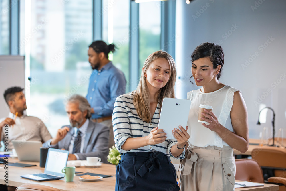 Obraz premium Two colleages discussing ideas using a tablet and computer. Cropped shot of colleagues working together on a digital tablet in a modern office. Businesswomen using digital tablet in office
