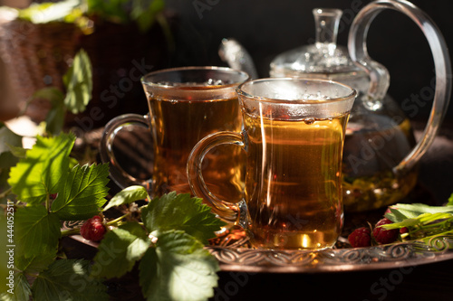 tea is poured into glass mugs. A teapot and a cup of tea stand on a copper tray next to raspberry leaves and berries