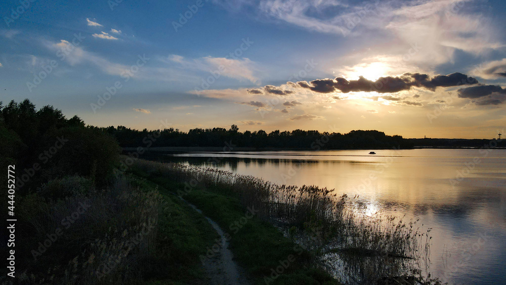 A picturesque sunset over the pond. Panoramic view of the countryside. Design of photo wallpapers, screensavers, covers.