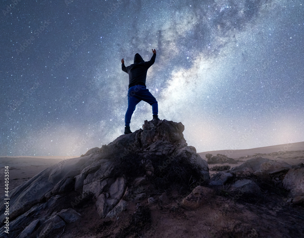 silhouette of a person on a rock with hands up staring at Milky Way, celebrating