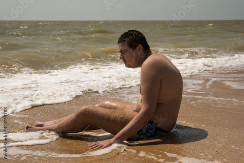 the guy is sitting on the seashore with his feet in the waves. the guy with autism