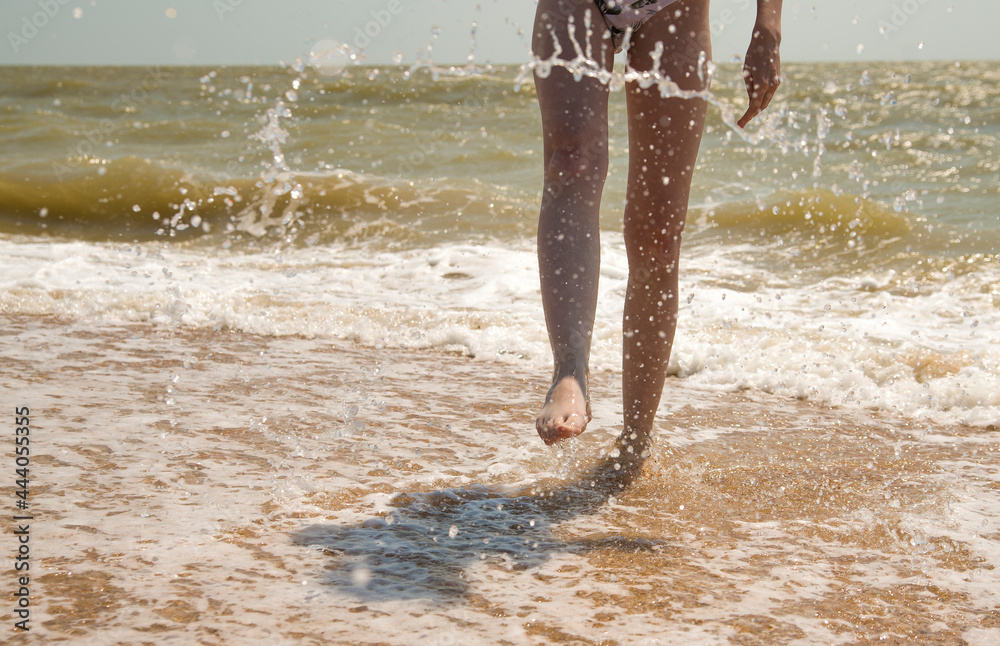 slender legs of a young girl splashing water from the sea
