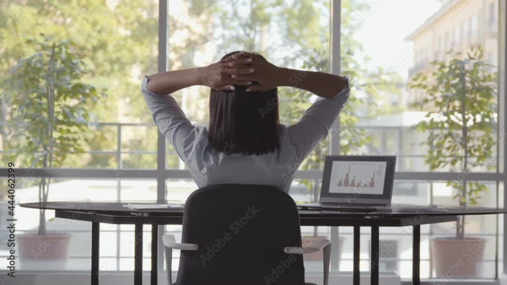Rear view of woman working on computer in office stretching at desk