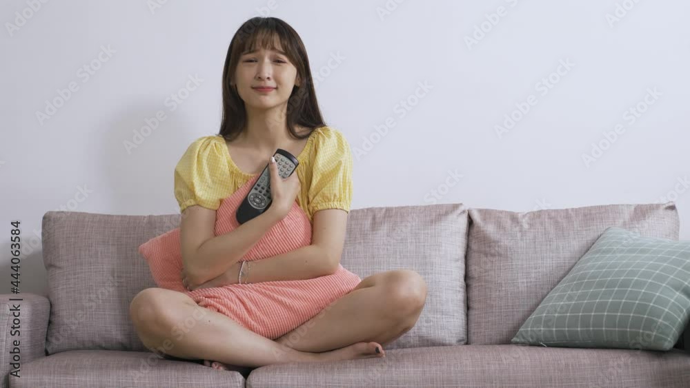 asian young lady hugging a pillow is cupping her face and covering her mouth in surprise while watching a touching romance on the couch over white background. asian young lady hugging a pillow is cupping her face and covering her mouth in surprise while watching a touching romance on the couch over white background.