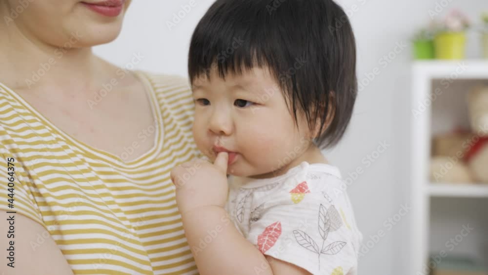 close up lovely asian young toddler is sucking her fingers in her mom’s cuddle and looking into the space with innocence at home. close up lovely asian young toddler is sucking her fingers in her mom’s cuddle and looking into the space with innocence at home.