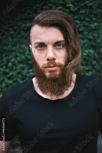 Boy with red hair and beard on a background of green plants