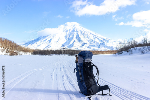 A blue tourist backpack stands on the snow against the background of the Koryaksky volcano at the 