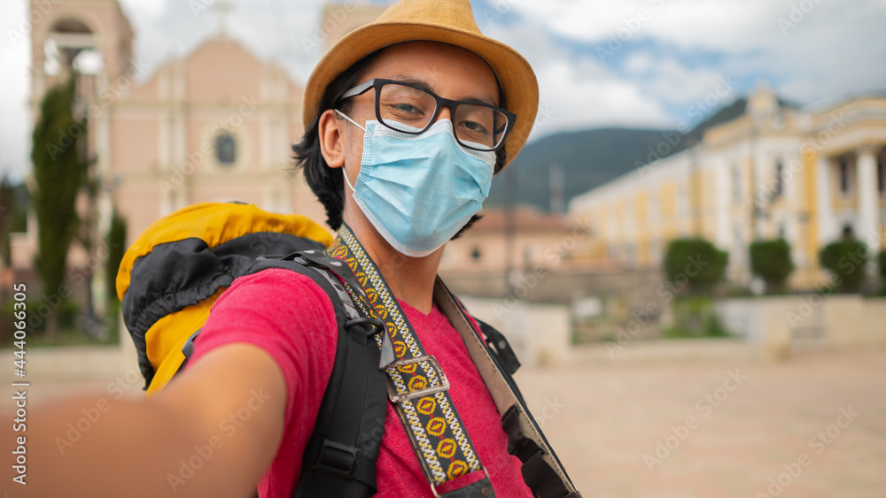 Obraz premium Portrait of a happy young man on vacation taking selfies in the park with the church as background.