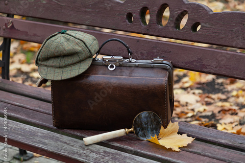 Fotografie, Obraz Travel bag and large magnifying glass stands on wooden bench
