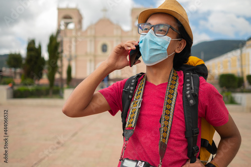 Portrait of a young man with a medical mask talking on a cell phone in front of Totonicapan church. 