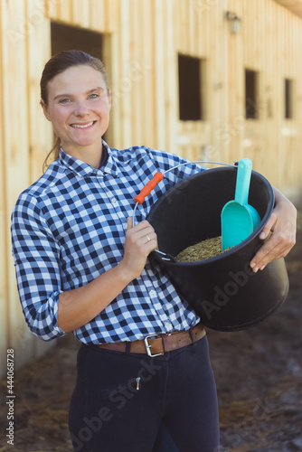 Horse owner holding a bucket full of grains and a scoop.Horse feeds. Girl in the horse ranch with rows of horse stall in the background. Time to feed the horses. photo