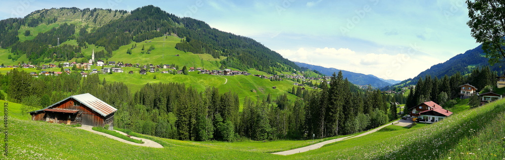 weites Panorama im Kleinwalsertal mit Dorf Mittelberg umrahmt von grünen Wiesen und Wald 