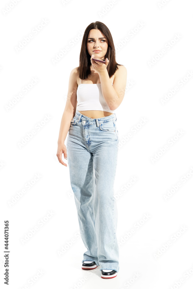 Displeased skeptical young gen Z stylish casual woman talking on cell phone speaker. Full body portrait isolated on white background Displeased skeptical young gen Z stylish casual woman talking on cell phone speaker. Full body portrait isolated on white background