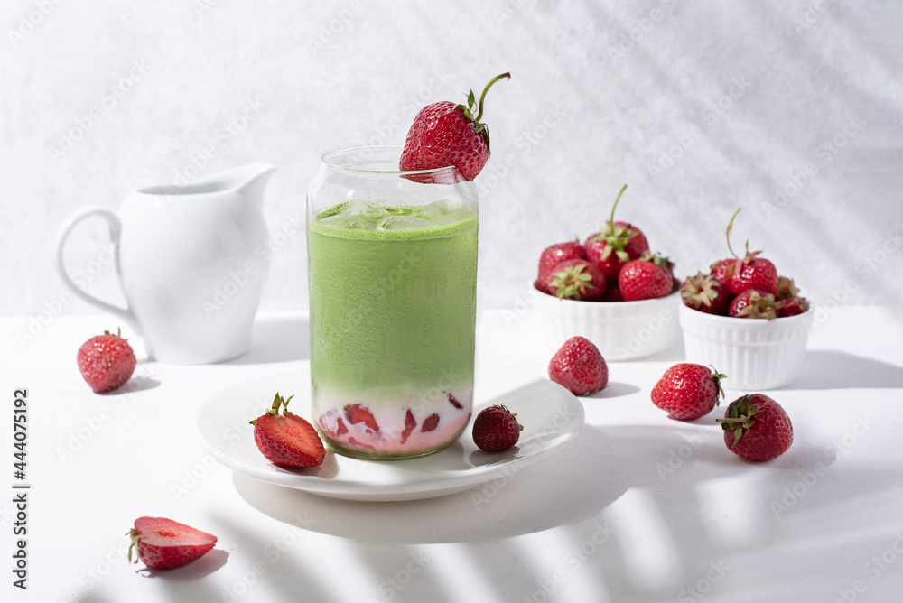 Glass with strawberry matcha latte with strawberries on a white background with beautiful shadows from the branches.