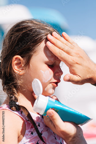 a parent puts sunscreen on a girl's face from a blue tube by the pool at a family hotel. 