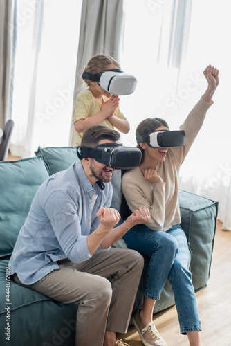 excited couple showing success gesture while gaming in vr headsets with daughter