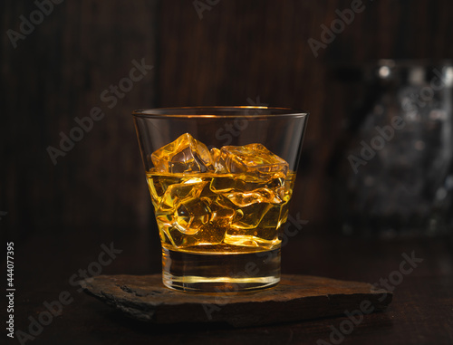 vaso de whisky con hielo encima de una mesita de madera rustica
