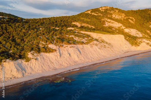 Aerial view of summer coastline with cliff, trees and quiet sea. Coastline with sunset