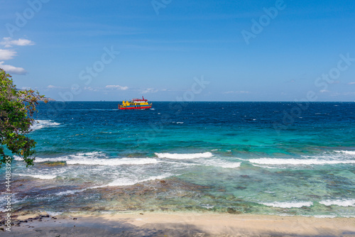 A view on a passing ferry during low tide on Blue Lagoon beach on a sunny day on Bali island in Indonesia.