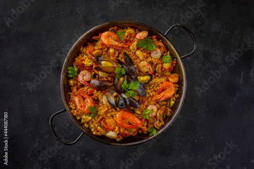 Traditional spanish seafood paella with rice, mussels, shrimps in a pan on dark background. view from above, flat lay