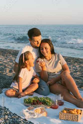 Family spending time together outdoor. Summer leisure concept. Picnic lunch with fruits by the seaside. Happy people eating healthy food and sitting on blanket on the beach.
