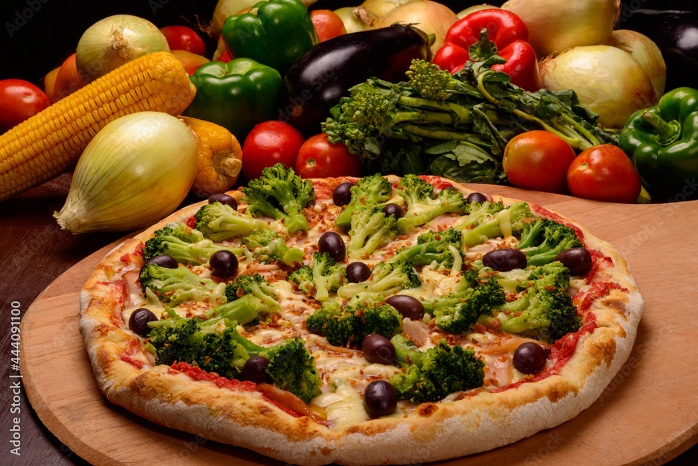 Broccoli pizza with black olives on wooden board and vegetables in the background. Broccoli pizza with black olives on wooden board and vegetables in the background.
