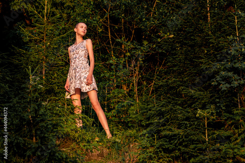 teenage girl in a summer dress in the forest lit by the rays of the sun