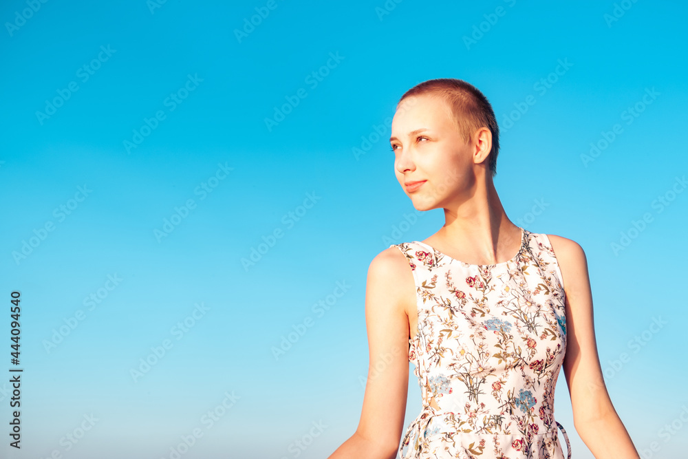 girl teenager in a dress with a short haircut looking into the distance, squinting at the sun, against the background of the sky girl teenager in a dress with a short haircut looking into the distance, squinting at the sun, against the background of the sky