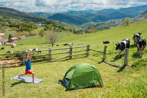 Healthy man doing yoga on meadow with tent photo