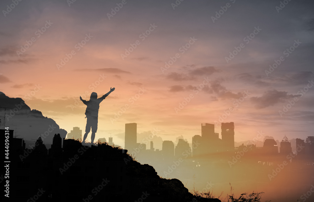 Man standing on top a mountain facing the city feeling happy and motivated 