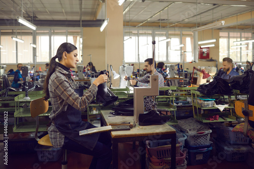 Young professional female shoemaker designer in apron working with leather material using crafting tools standing at workplace. Footwear factory  fashion shoe production industry concept