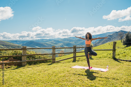 Woman practicing yoga on green yard in mountains photo