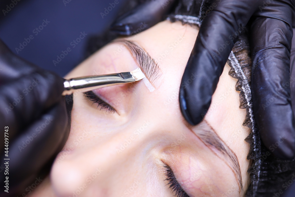 Obraz premium the hands of the tattoo artist close up emphasize the contour of the eyebrows with a brush