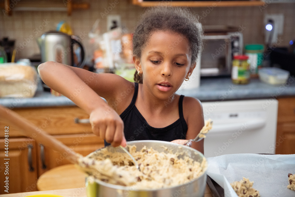 Young girl scooping spoonfuls of dough onto a tray Young girl scooping spoonfuls of dough onto a tray