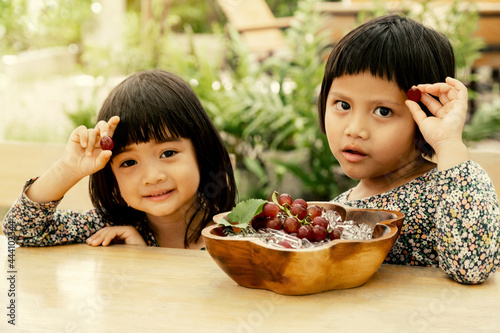 Happy baby and kid wearing twin clothes sitting on the table with a plate of grapes freeze in ice  eat healthy fruit childhood lifestyle