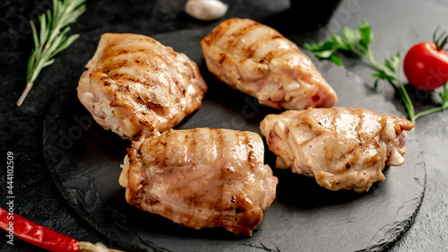 grilled skinless chicken thighs with spices and herbs on a stone background photo