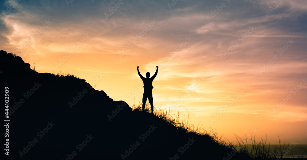 Strong young man reaching the top of a mountain with fist in the air. 