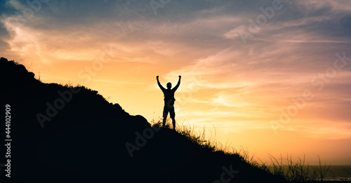Strong young man reaching the top of a mountain with fist in the air. 