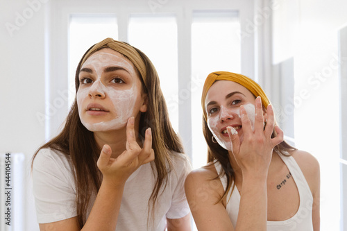 Two girl friends apply clay mask on face at home