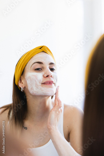 Pretty girl applying beauty mask on her face at home.