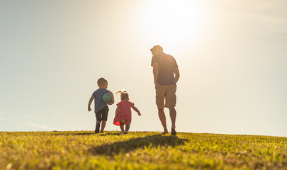 Happy father and his children running together in a open field. 