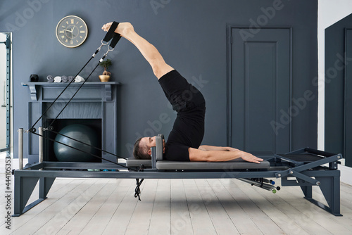 Man doing exercises on pilates reformer in gym photo