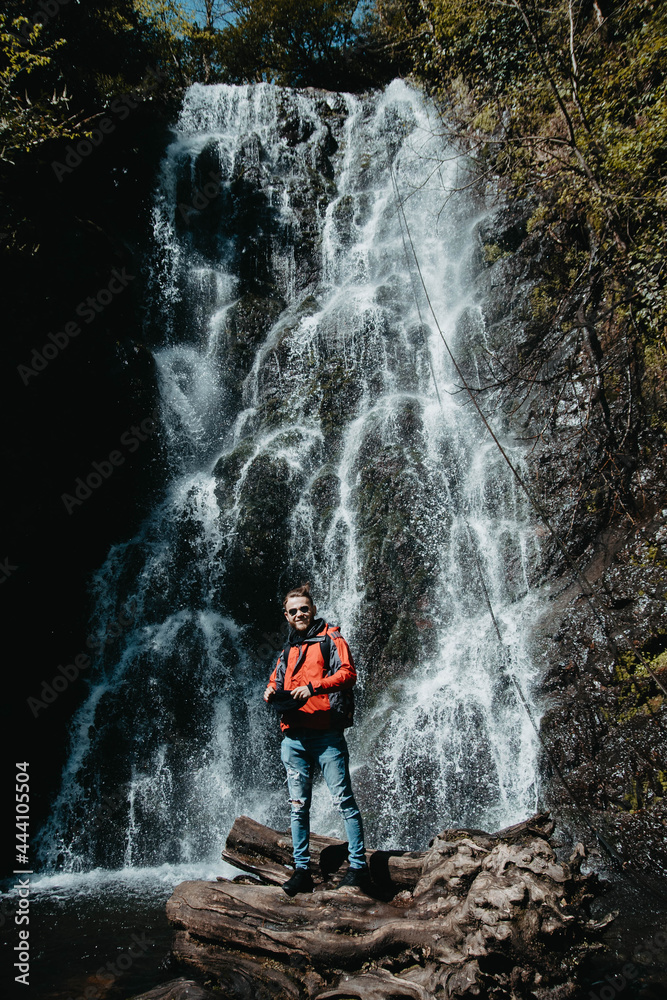Obraz premium male traveler stands at a waterfall in the forest