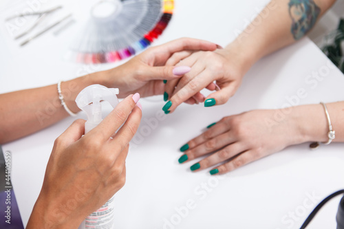 Cose up of manicurist disinfecting hands of female client