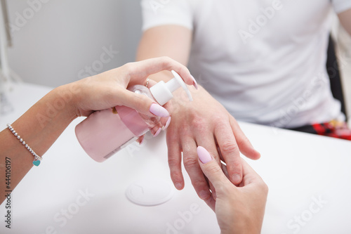 Close up of manicurist applying hand cream on male hands