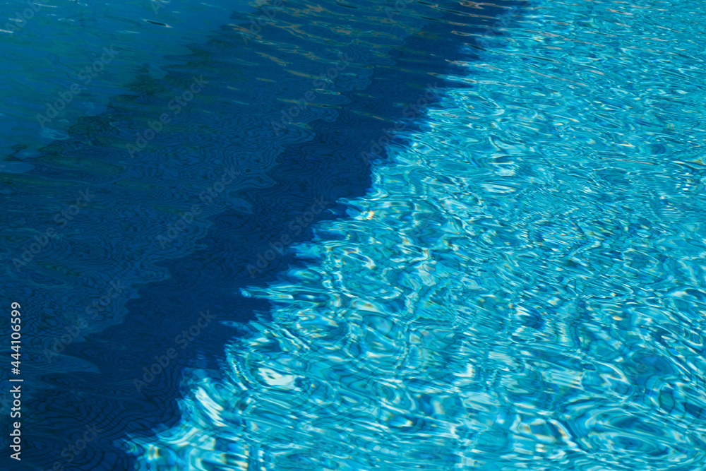 Obraz premium A two colored light and dark blue water with ripples and sunny reflections in a swimming pool.