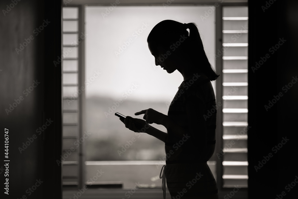 Silhouette of sad young woman using smartphone indoors 